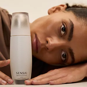 Close up of person laying their head and hands on surface next to Absolute Silk Micro Essence in Lotion